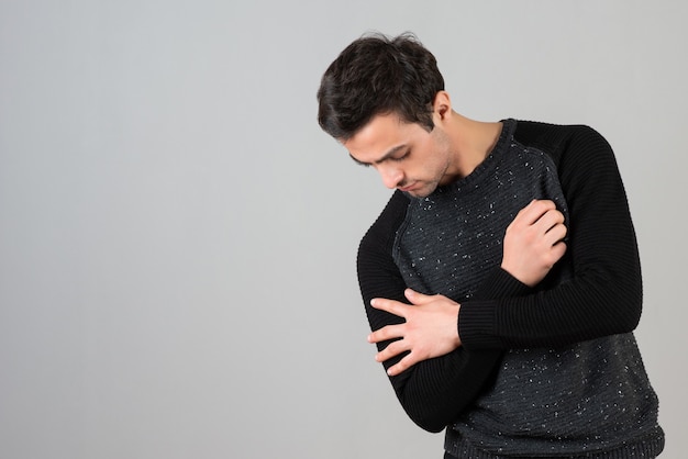 Portret van een jonge man in vrijetijdskleding die naar beneden kijkt op grijze muur