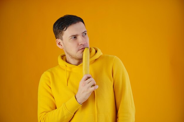 Portret van een jonge man met banaan op gele achtergrond Grappige kerel in gele hoodie poseren met fruit