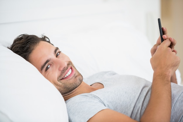 Portret van een jonge man met behulp van mobiele telefoon op bed