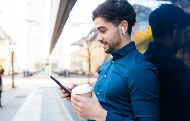 Portret van een jonge man met behulp van zijn mobiele telefoon en met een kopje koffie