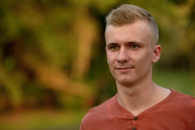 Portret van een jonge man met blond haar in het park buiten