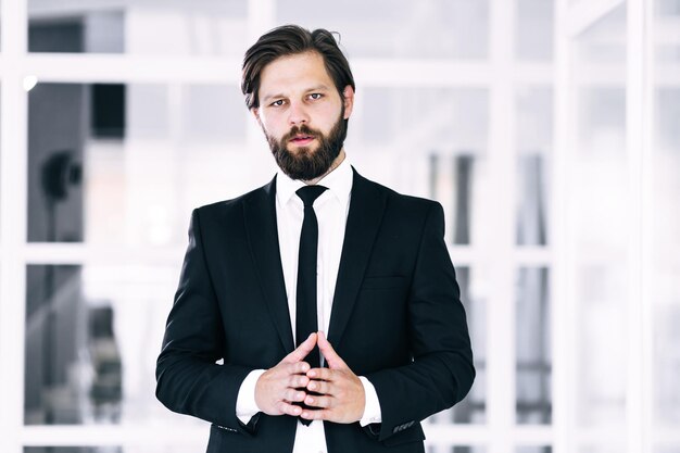 Portret van een jonge man met gekruiste armen in een pak op de achtergrond van het kantoor