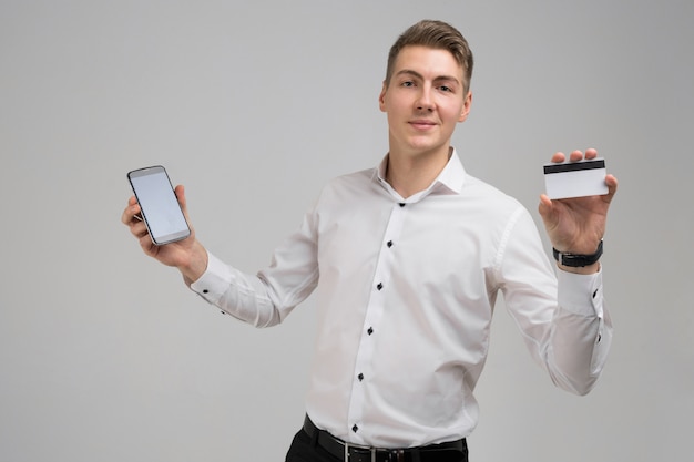 Portret van een jonge man met mobiele telefoon en betaalpas in zijn handen op wit