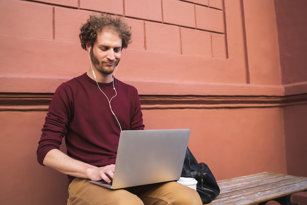 Portret van een jonge man met zijn laptop terwijl hij buiten zit