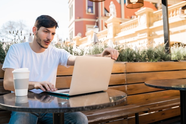 Portret van een jonge man met zijn laptop zittend in een coffeeshop. Technologie en levensstijlconcept.