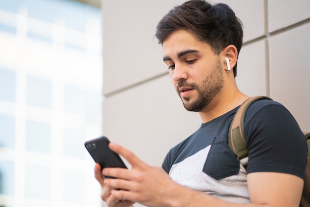 Portret van een jonge man met zijn mobiele telefoon terwijl hij buiten op straat staat. Stedelijk concept.