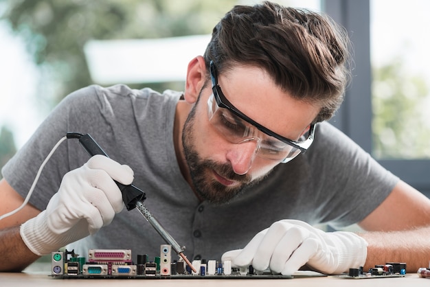 Foto portret van een jonge man solderen computer circuit in werkplaats