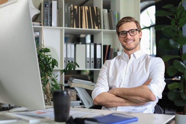 Portret van een jonge man zit aan zijn bureau op kantoor.