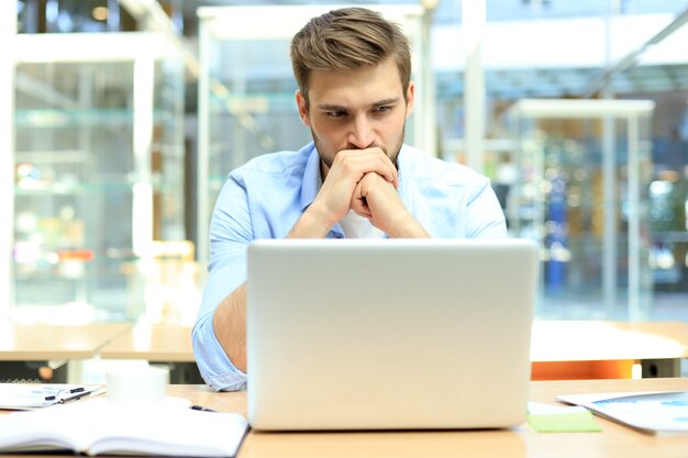 Portret van een jonge man zit aan zijn bureau op kantoor.