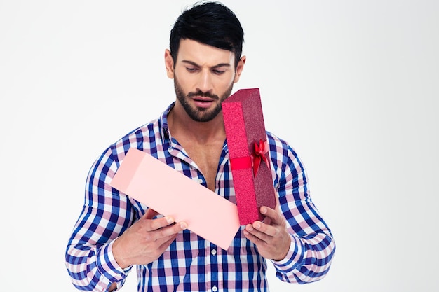 Portret van een jonge mens die giftdoos opent die op een witte muur wordt geïsoleerd