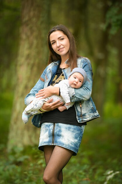Portret van een jonge moeder met een baby op straat. Baby op de handen van een jonge lachende moeder in een lente steegje.