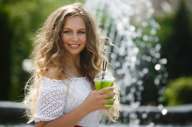 Portret van een jonge mooie aantrekkelijke vrouw buitenshuis in de zomer met een glas ijskoud sap of drankje. Mooi meisje buiten met verse mojito