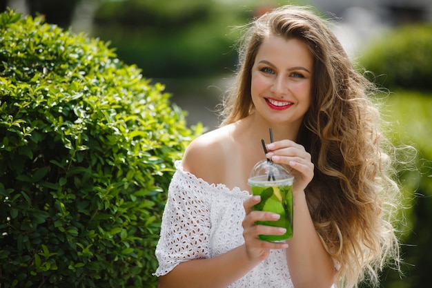 Portret van een jonge mooie aantrekkelijke vrouw buitenshuis in de zomer met een glas ijskoud sap of drankje. Mooi meisje buiten met verse mojito