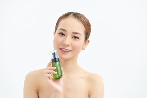 Portret van een jonge, mooie aziatische vrouw die een groene fles voor cosmetisch product bij de hand laat zien