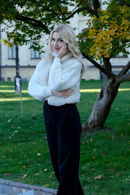 Portret van een jonge mooie blonde met lang haar in een witte trui en jas in een zonnige herfst in een stadspark