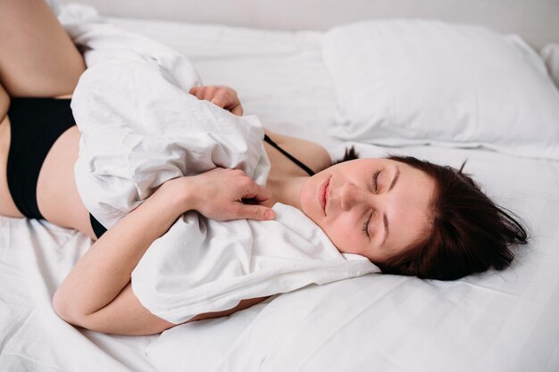 Portret van een jonge mooie brunette die in bed ligt en ondergoed draagt