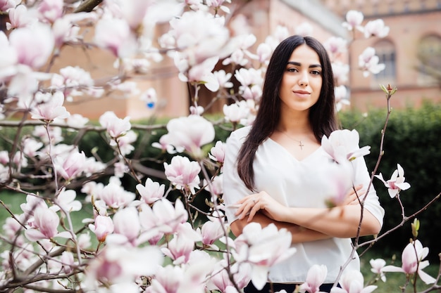 Portret van een jonge mooie dame in de buurt van magnoliaboom met bloemen.