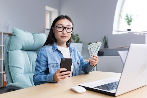 Portret van een jonge, mooie freelancer-vrouw die naar de camera kijkt en glimlacht terwijl ze de telefoon vasthoudt en