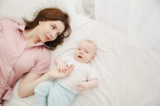 Portret van een jonge mooie Kaukasische moeder en baby op het bed. Bovenaanzicht. Kopieer ruimte