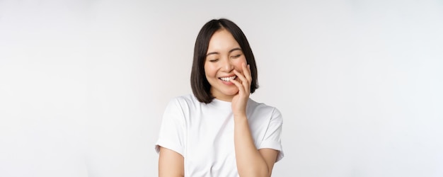 Portret van een jonge, mooie, Koreaanse meid die lacht en glimlacht en er koket uitziet tegen een witte achtergrond