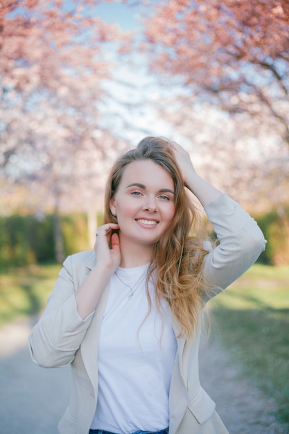 Portret van een jonge mooie, krullende vrouw in een bloeiende sakuratuin. Voorjaar.