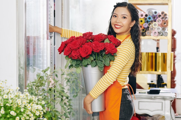 Portret van een jonge, mooie Vietnamese bloemist die een emmer verse rode rozen in een bloemendisplay zet