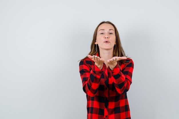 Foto portret van een jonge, mooie vrouw die een luchtkus met pruilende lippen in een casual shirt verzendt en er vrolijk vooraanzicht uitziet