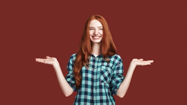 Portret van een jonge mooie vrouw die jongleert met de handpositie voor het gooien van voorwerpen, kijkend naar de camera met een glimlach, geïsoleerd op rode achtergrond