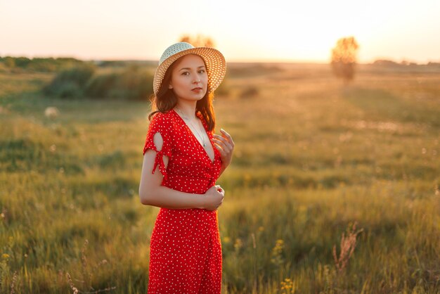 Portret van een jonge mooie vrouw in een rode jurk en een zomer panama hoed bij zonsondergang.