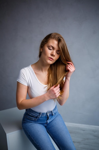 Portret van een jonge, mooie vrouw met blond haar van Europees uiterlijk Gekleed in een wit T-shirt Emotionele foto van een persoon