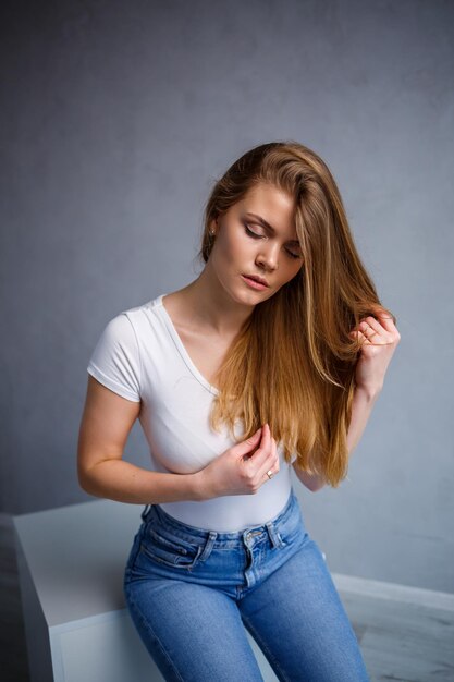 Portret van een jonge, mooie vrouw met blond haar van Europees uiterlijk Gekleed in een wit T-shirt Emotionele foto van een persoon