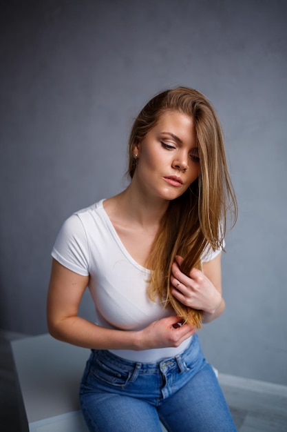 Portret van een jonge, mooie vrouw met blond haar van Europees uiterlijk Gekleed in een wit T-shirt Emotionele foto van een persoon