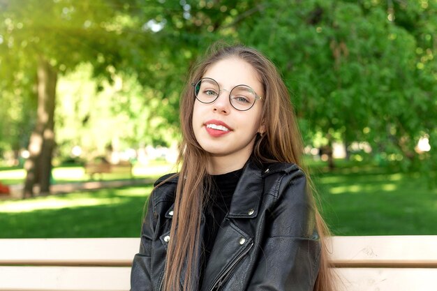 Portret van een jonge mooie vrouw met een bril in een zomers groen park zittend op een bankje