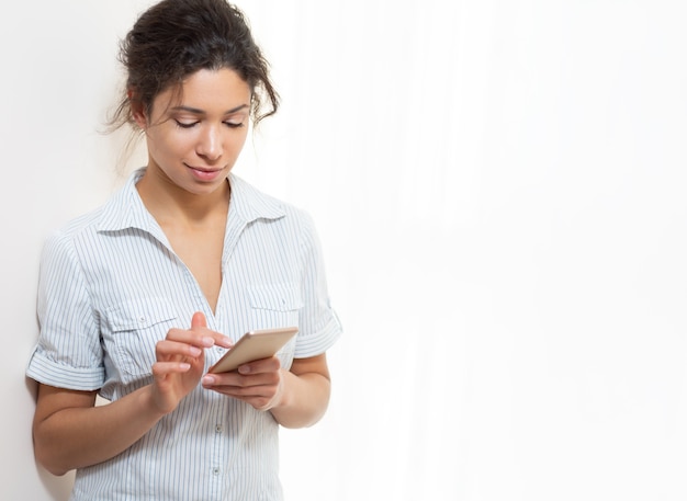 Portret van een jonge mooie vrouw met een telefoon dichtbij de witte muur