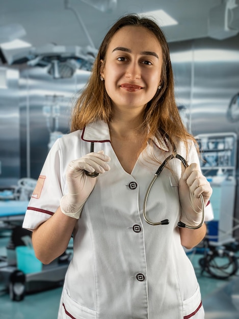 Portret van een jonge, mooie vrouwelijke arts of medisch assistent die een wit uniform draagt met een stethoscoop Werk in een moderne operatiekamer