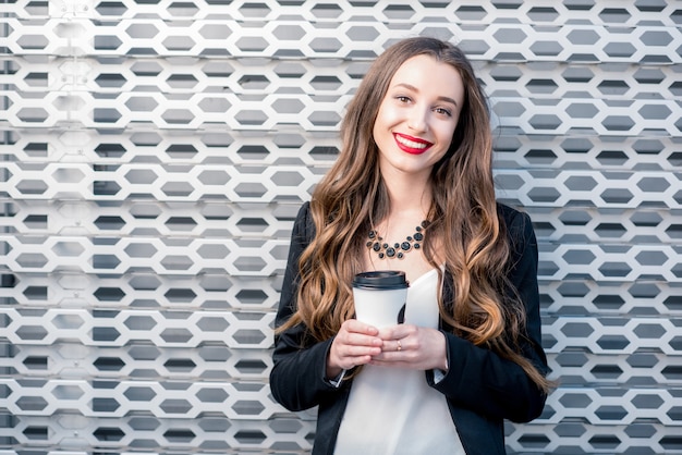 Portret van een jonge mooie zakenvrouw met koffie op de achtergrond van de metalen muur