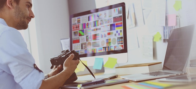 Portret van een jonge ontwerper die in een grafische studio voor een laptop en computer zit terwijl hij online werkt