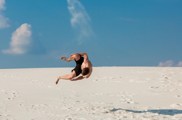 Portret van een jonge parkour-man die flip of salto op het zand doet.