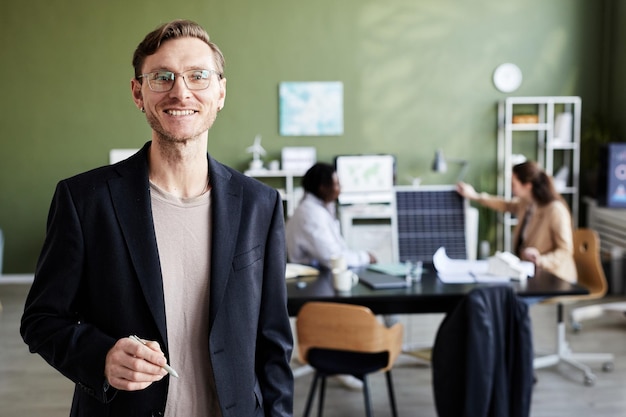 Portret van een jonge professionele ingenieur die naar de camera glimlacht terwijl hij op kantoor staat