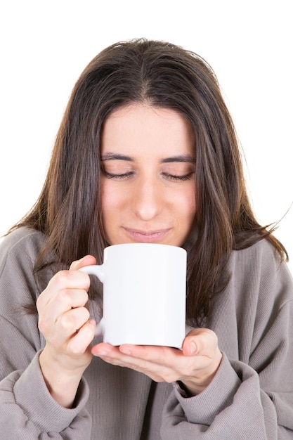 Portret van een jonge schattige bruine vrouw die geniet van haar warme, gezellige warme drank in een grote lege witte mok