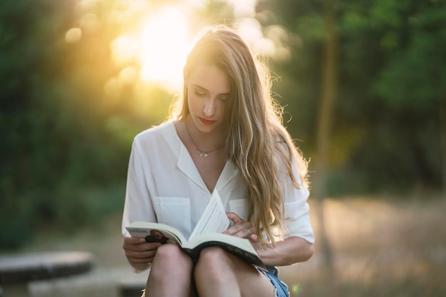 Portret van een jonge Spaanse vrouw die in een park zit en een boek leest op een zonnige dag