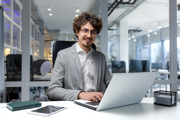 Portret van een jonge succesvolle zakenman financier man binnen kantoor op werkplek zittend met behulp van