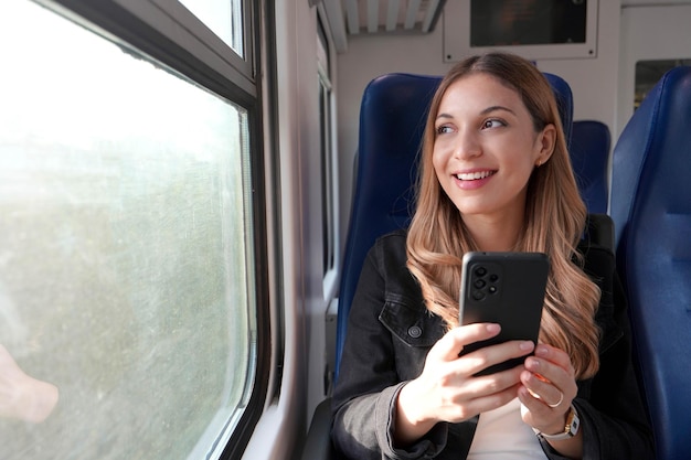 Portret van een jonge tevreden vrouw die met het openbaar vervoer reist terwijl ze een mobiele telefoon vasthoudt en gedachteloos ontspant