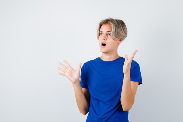 Portret van een jonge tienerjongen die een overgavegebaar toont in een blauw t-shirt en een bang vooraanzicht ziet