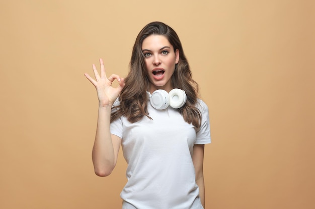 Portret van een jonge vrolijke lachende vrouw die een goed gebaar toont, met copyspace over een beige achtergrond.