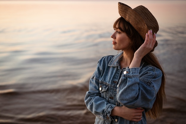Portret van een jonge vrouw aan zee in een hoed bij zonsondergang in de zomer