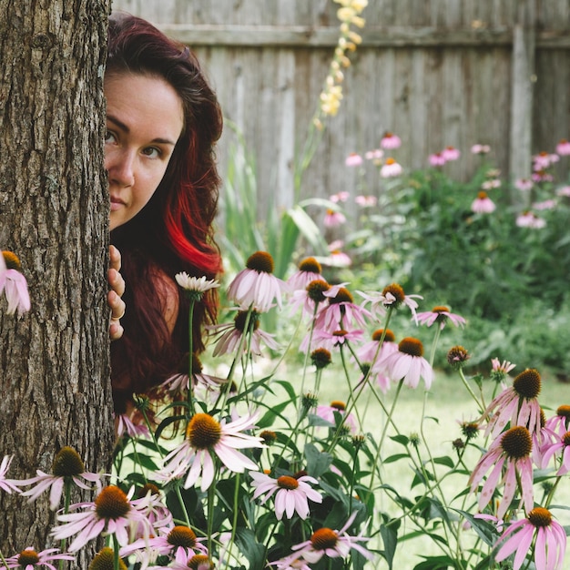 Foto portret van een jonge vrouw die achter een boomstam in het park staat