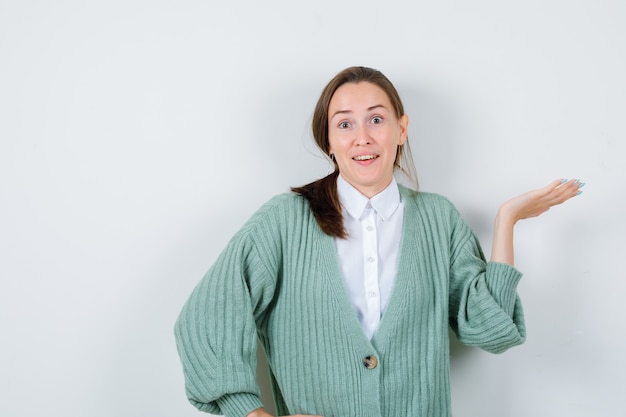 Portret van een jonge vrouw die de palm opzij spreidt in een blouse, een vest en een verbaasd vooraanzicht kijkt