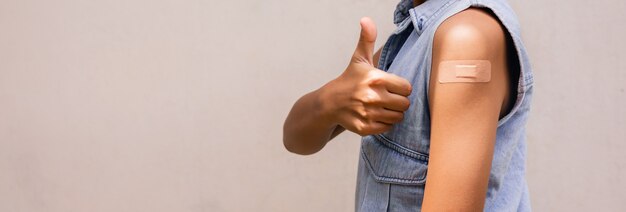 Portret van een jonge vrouw die duimen laat zien na het krijgen van een vaccin. staande op een witte achtergrond