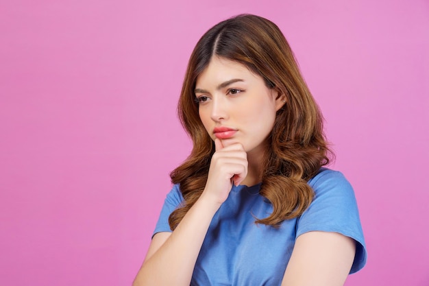 Portret van een jonge vrouw die een casual t-shirt draagt, denken en verbeeldingskracht, geïsoleerd over roze achtergrond